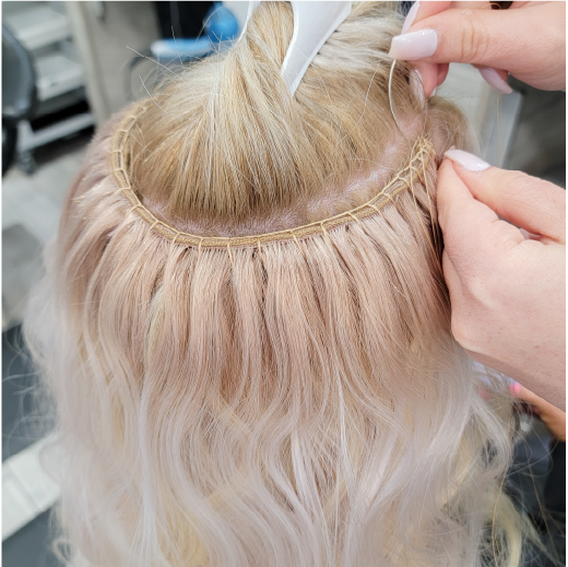 Stylist sewing blonde hair weft onto the extension track using needle and thread