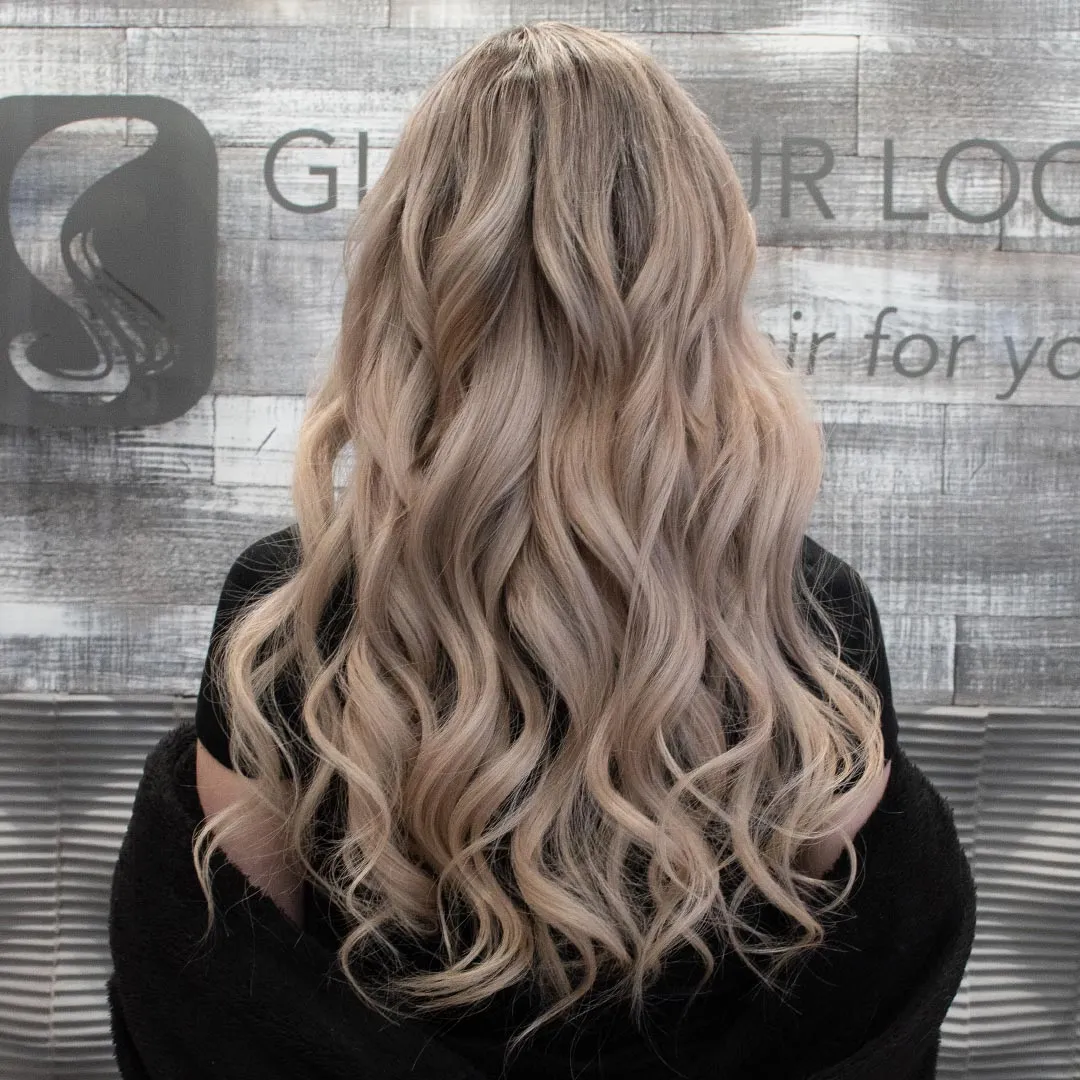 Back view of ash blonde weft hair extensions with long layered waves and natural finish